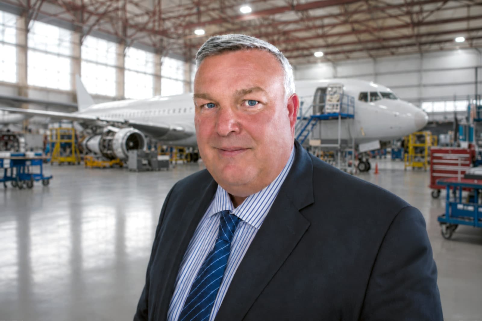 Nigel Brown in an aircraft maintenance hangar with a commercial aircraft and aerospace engineering equipment in the background.